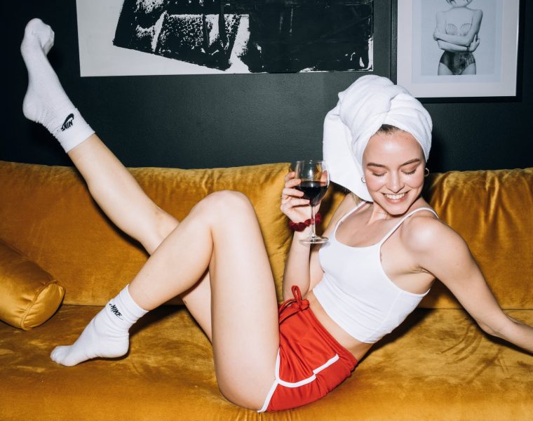 Alfa žene zodijaka, young woman sitting on a yellow sofa while holding a wine glass with red wine