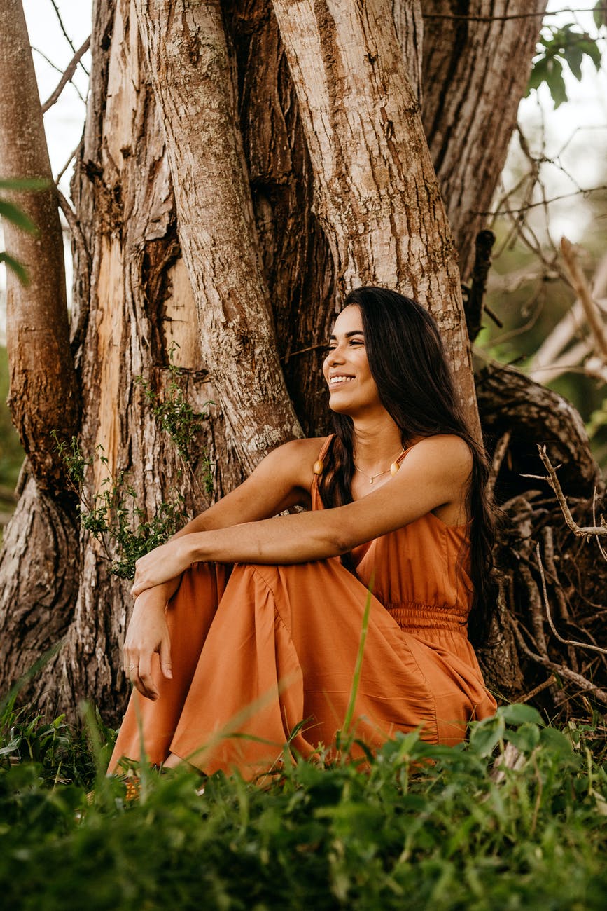 joyful woman in stylish maxi dress resting near old tree