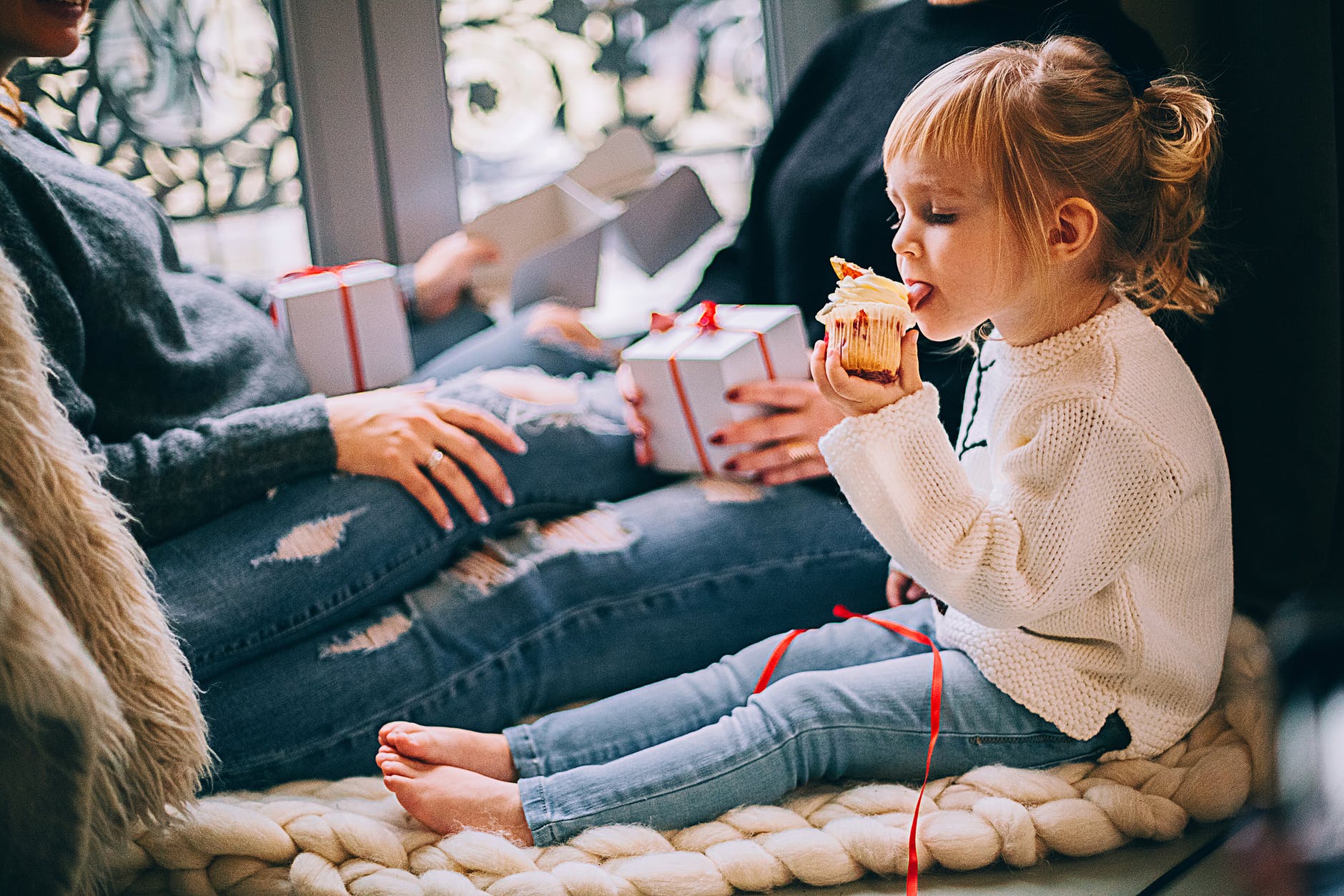 girl eating cupcake while sitting beside woman in blue denim distressed jeans