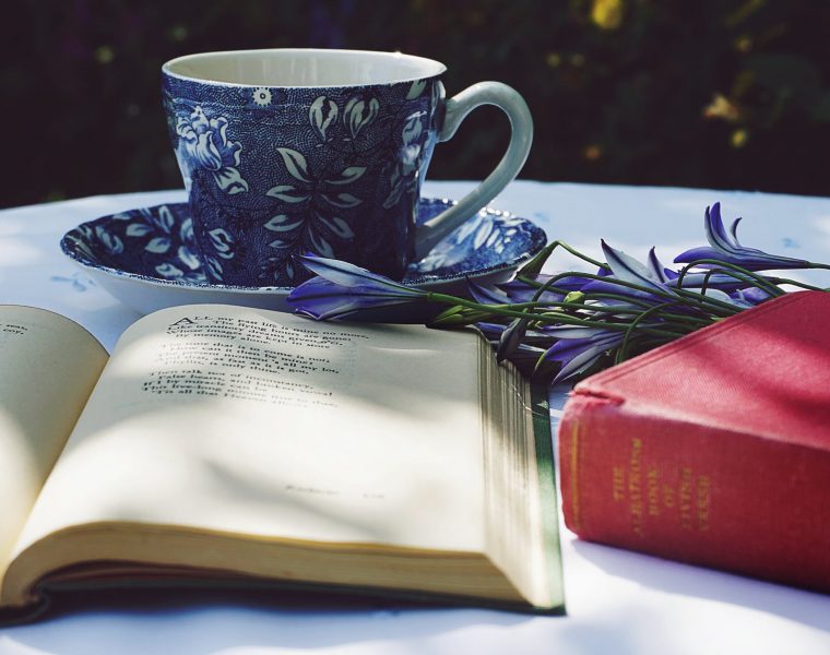 zbirka poezije "Tiho sunce" , book opened on top of white table beside closed red book and round blue foliage ceramic cup on top of saucer