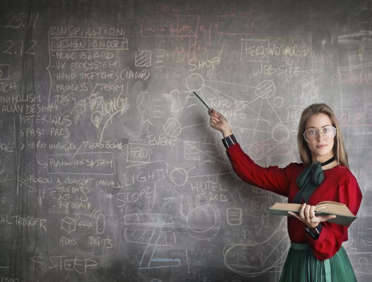 strict female teacher with book pointing at scribbled blackboard