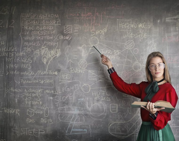 strict female teacher with book pointing at scribbled blackboard