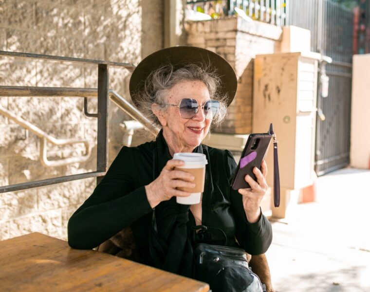 Starica (92), woman in black using her smartphone while having coffee