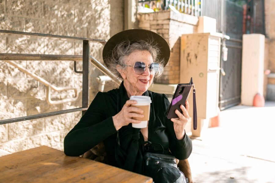 Starica (92), woman in black using her smartphone while having coffee
