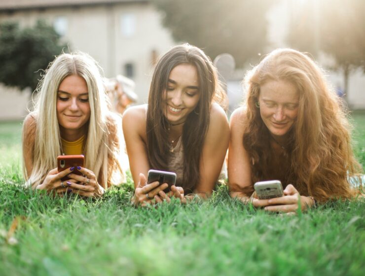Moderne tehnologije female friends browsing smartphone on lawn