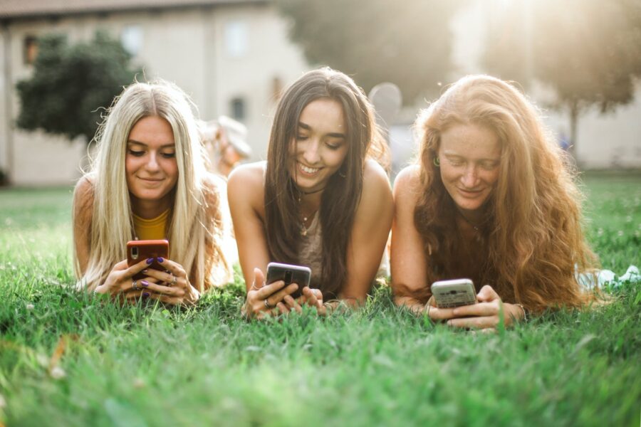 Moderne tehnologije female friends browsing smartphone on lawn