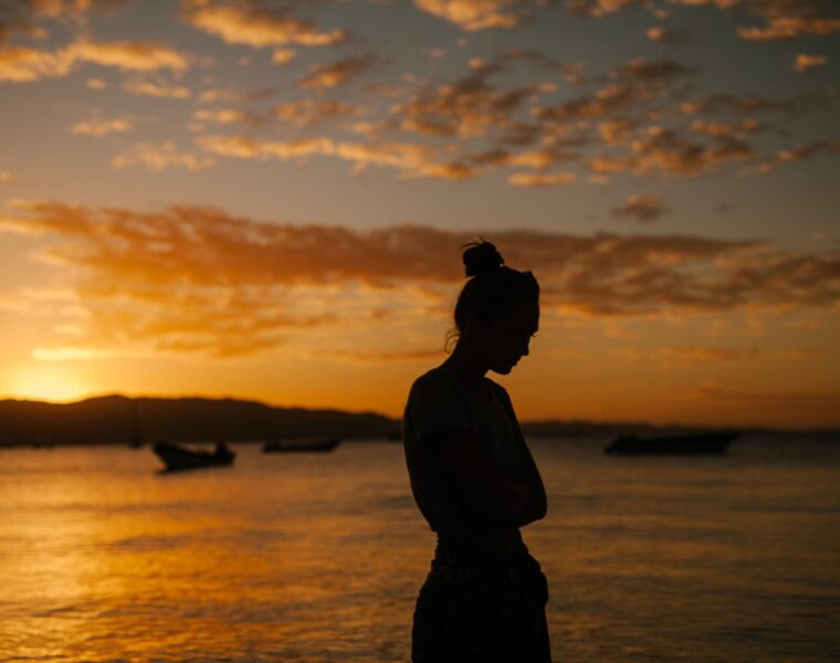 Oslobođenje od krivnje, sad woman standing on coast of sea at sunset
