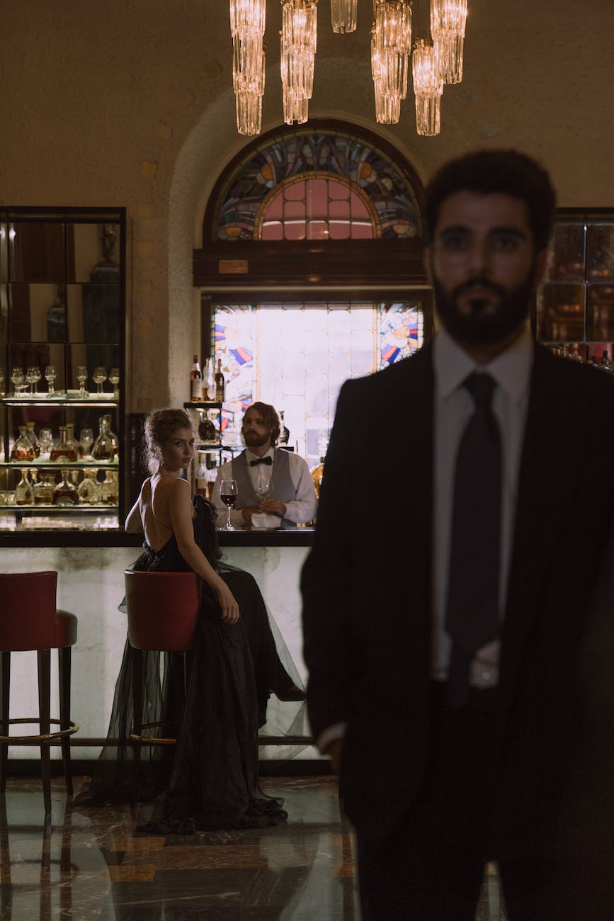 woman in black dress sitting on a chair while looking at a man in black suit standing