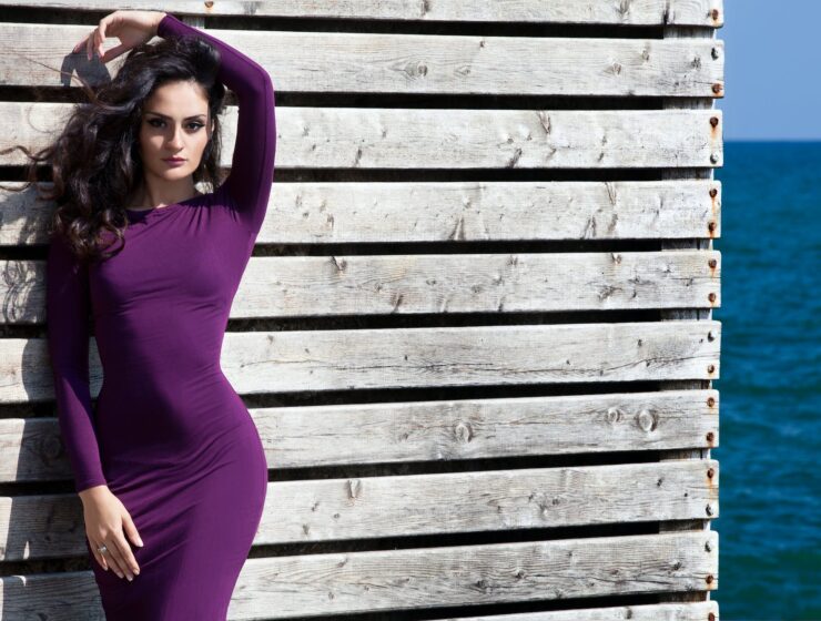 Glagol woman in purple long sleeve dress standing beside white wooden wall